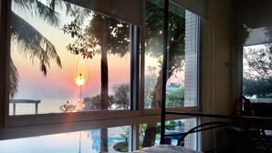 Ein Schlafzimmer mit großem Fenster, das einen Blick auf einen Pool und Palmen mit Sonnenuntergang bietet.