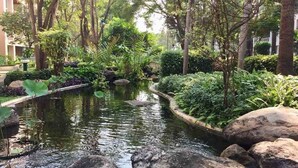Ein friedlicher Garten mit Teich, umgeben von üppiger Bepflanzung und großen Steinen.