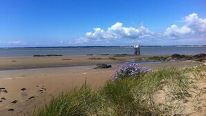 Ein Strand mit einem Felsen und einer im Hintergrund stehenden, auf Stelzen gebauten Konstruktion.