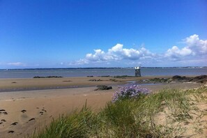 Ein Strand mit einem Felsen und einer im Hintergrund stehenden, auf Stelzen gebauten Konstruktion.