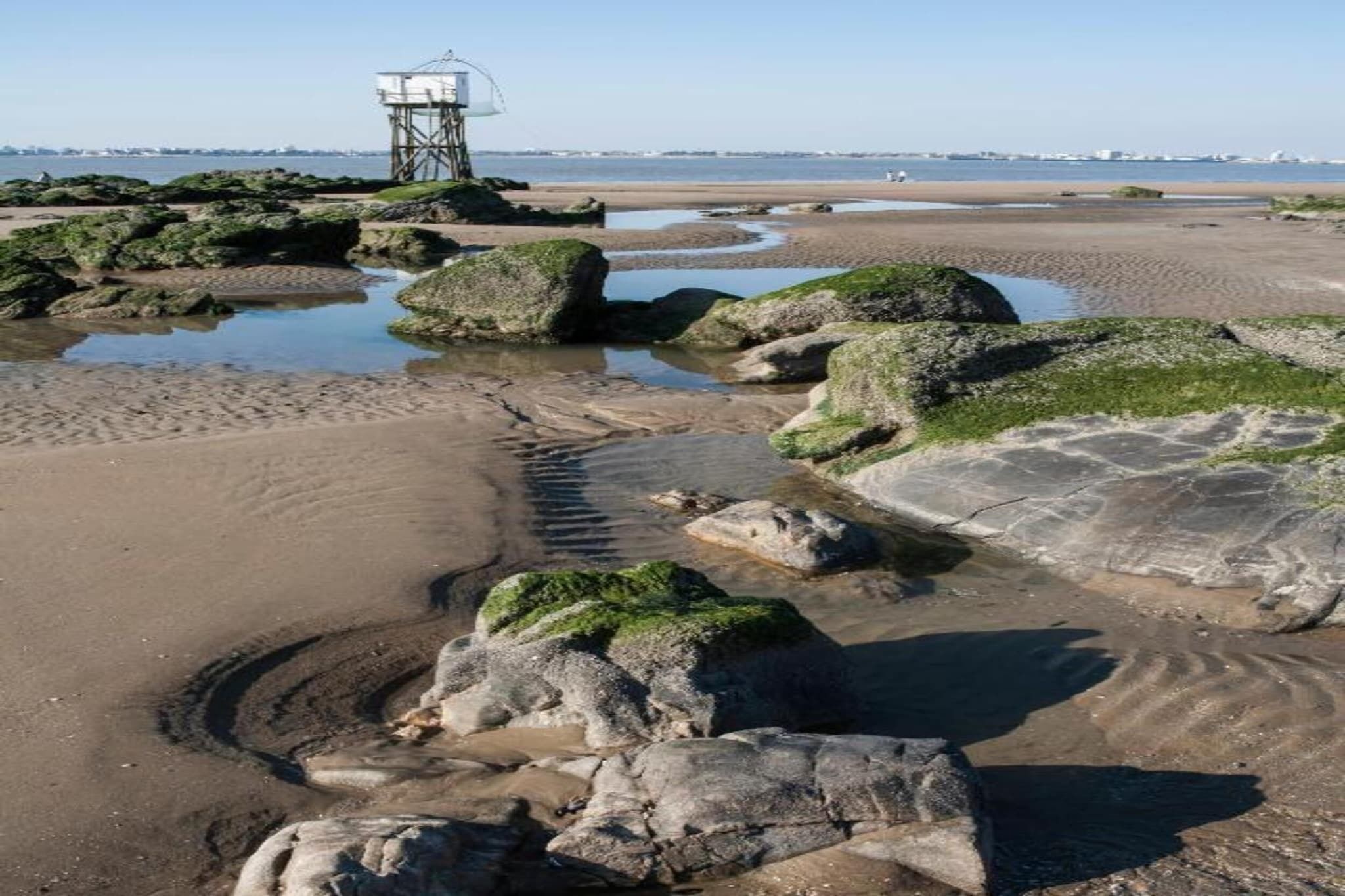 A coastal landscape with rocky terrain, a sandy beach, and a lighthouse in the distance.