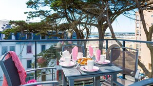 Ein Balkon mit Tisch für zwei Personen, Blick auf Strand und Gebäude.