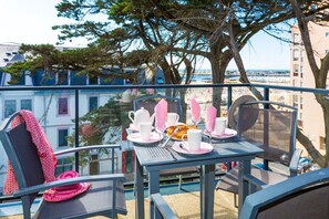Ein Balkon mit Tisch für zwei Personen, Blick auf Strand und Gebäude.