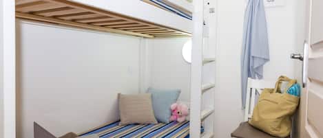 A bunk bed with a laptop on the lower bunk, a teddy bear, and a bag on a chair.