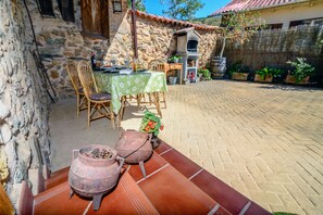 A rustic outdoor dining area with stone walls, a brick floor, and a table set with chairs and a green tablecloth.