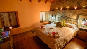 Une chambre avec un mur en pierre, des poutres apparentes en bois au plafond, un lit avec des serviettes, une table de chevet et une fenêtre avec des rideaux.