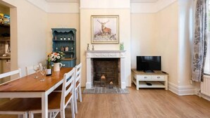 A living room with a fireplace, a television, a dining table with chairs, and a bookshelf. - Bikki Apartments, Bikki Apartments (Harrow)