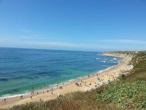 A beach with clear blue water, sandy shore, and a few umbrellas.