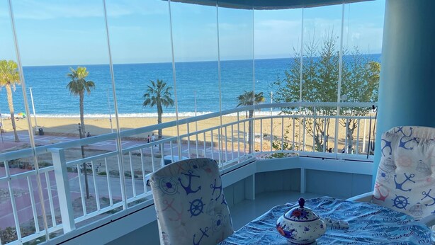 Un balcone con vista sulla spiaggia e sull'oceano, arredato con un tavolo e sedie, e una ventola a soffitto.