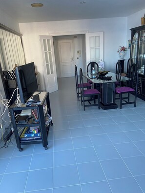 A dining area with a glass table and chairs, a television on a stand, and a cabinet with glass doors.