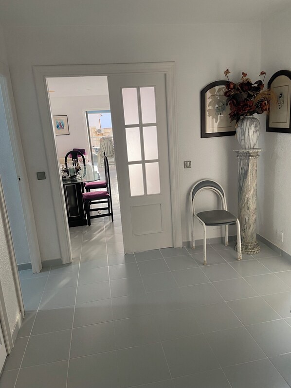 A hallway with a white door, a chair, a marble column, and framed pictures on the wall. - Aguilas Playa residence (Águilas)