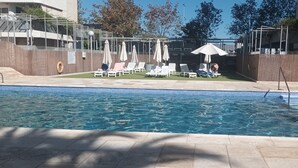Una piscina con lettini e ombrelloni, circondata da una recinzione in legno e edifici.