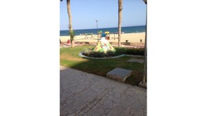 Un vialetto lastricato conduce a una spiaggia con palme e una colorata scultura a forma di uccello.