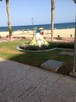 A paved walkway leading to a beach with palm trees and a colorful bird sculpture.