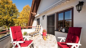 A terrace with two red chairs, a table with a white tablecloth, and a window with a view of trees. - Vacation apartment Ziske, Germany (Bad Wildungen)