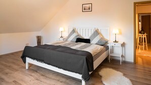 A bedroom with a bed, two bedside tables, a lamp on each table, a white wall, a framed picture, and a wooden floor. - Vacation apartment Ziske, Germany (Bad Wildungen)