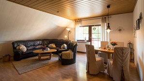 A cozy living room with a black leather sofa, a wooden coffee table, and a dining area with a table and chairs. - Vacation apartment Ziske, Germany (Bad Wildungen)