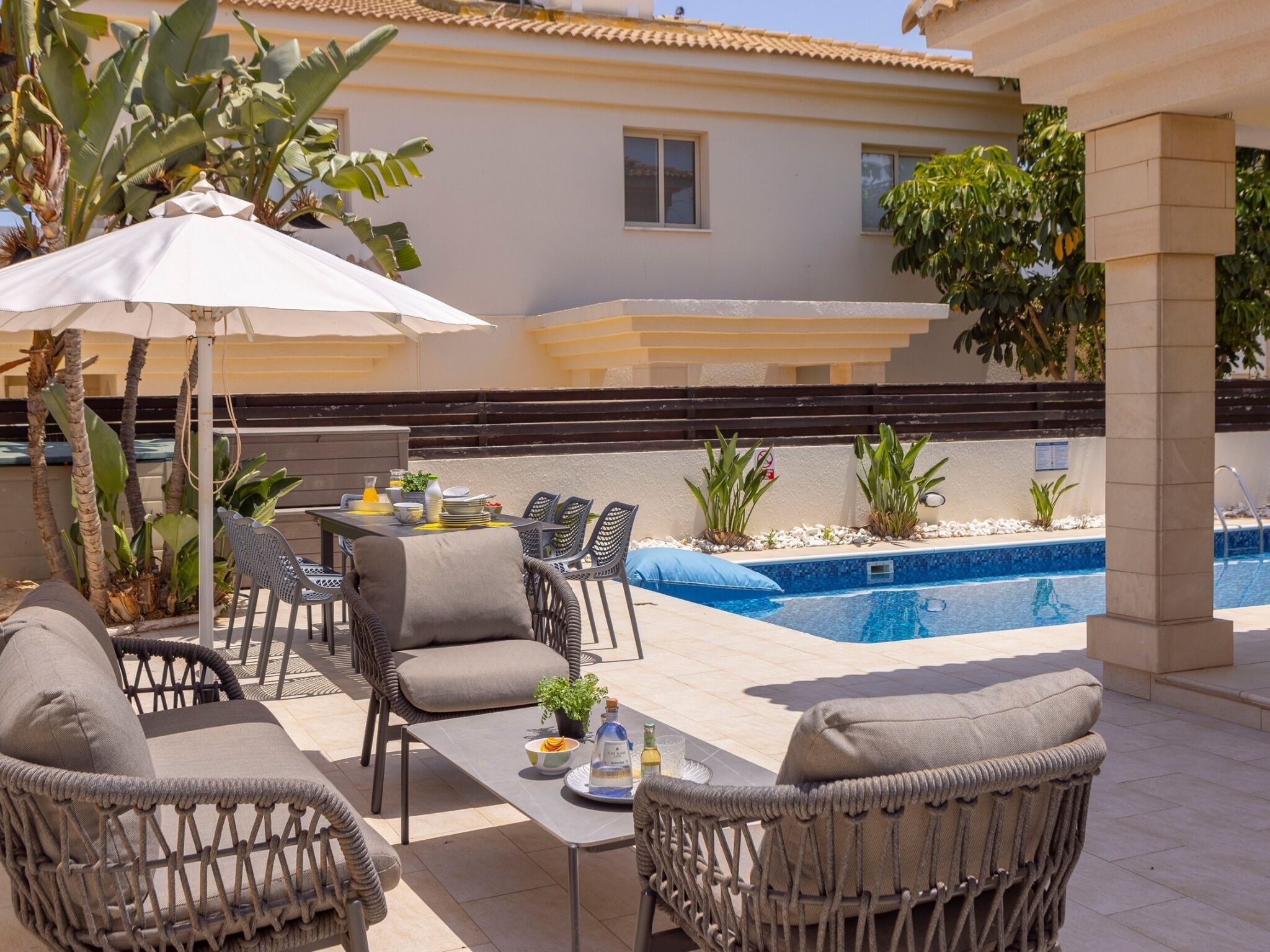 An outdoor patio with wicker furniture, a pool, and tropical plants.
