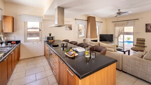 Een moderne keuken met een centraal eiland, houten keukenkastjes en een zithoek met een bank en televisie.