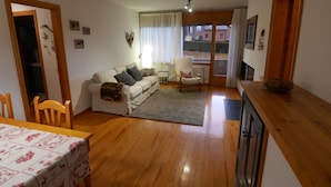 A cozy living room with a sofa, a chair, a dining table with a tablecloth, and a view through a window. - Cozy apartment in Alp with garden and parking, 10 minutes from the ski slopes! (Alp)