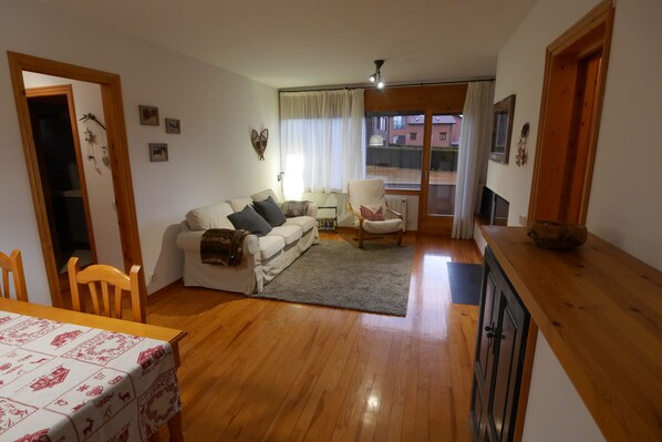 A cozy living room with a sofa, a chair, a dining table with a tablecloth, and a view through a window. - Cozy apartment in Alp with garden and parking, 10 minutes from the ski slopes! (Alp)