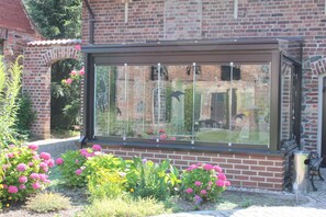 Ein Wintergarten mit Glasverkleidung, Ziegelmauern und einem Garten mit rosa Blüten.