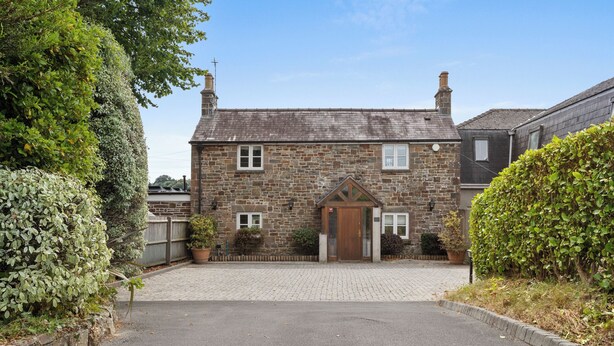 A stone house with a paved driveway, a wooden door, and a small garden area.