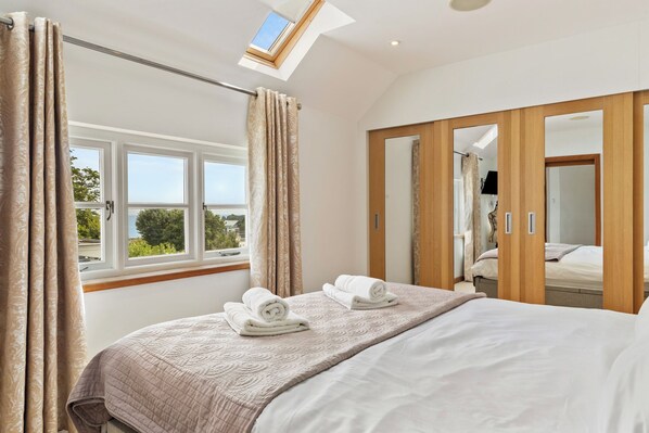 Un dormitorio con cama, dos toallas enrolladas, una ventana con cortinas y vistas al exterior.