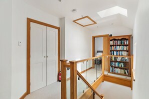 A staircase with wooden railings leading to a landing with a bookshelf and a white door.