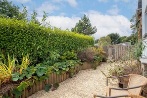 A garden with a wooden fence, gravel path, and a wicker chair.