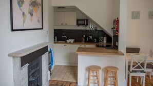A compact kitchen with a microwave, stove, and wooden bar counter. There are two stools and a dining table with chairs. A world map is displayed on the wall. - Toothbrush Apartments - Central Ipswich - Fonnereau Rd (Ipswich)