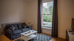 A modern living room with a grey sofa, a white coffee table, and a large window with curtains. - Toothbrush Apartments - Central Ipswich - Fonnereau Rd (Ipswich)