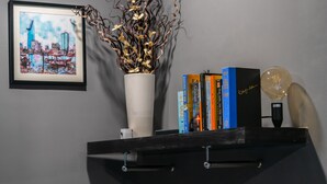 A bookshelf with books, a vase with decorative branches, and a framed cityscape painting.