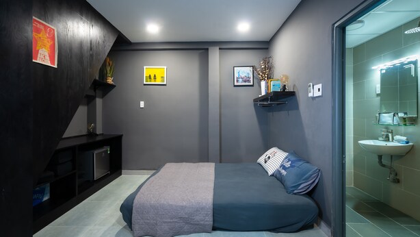 A modern bedroom with a bed, a small shelf with decorative items, and a bathroom with a sink and mirror.