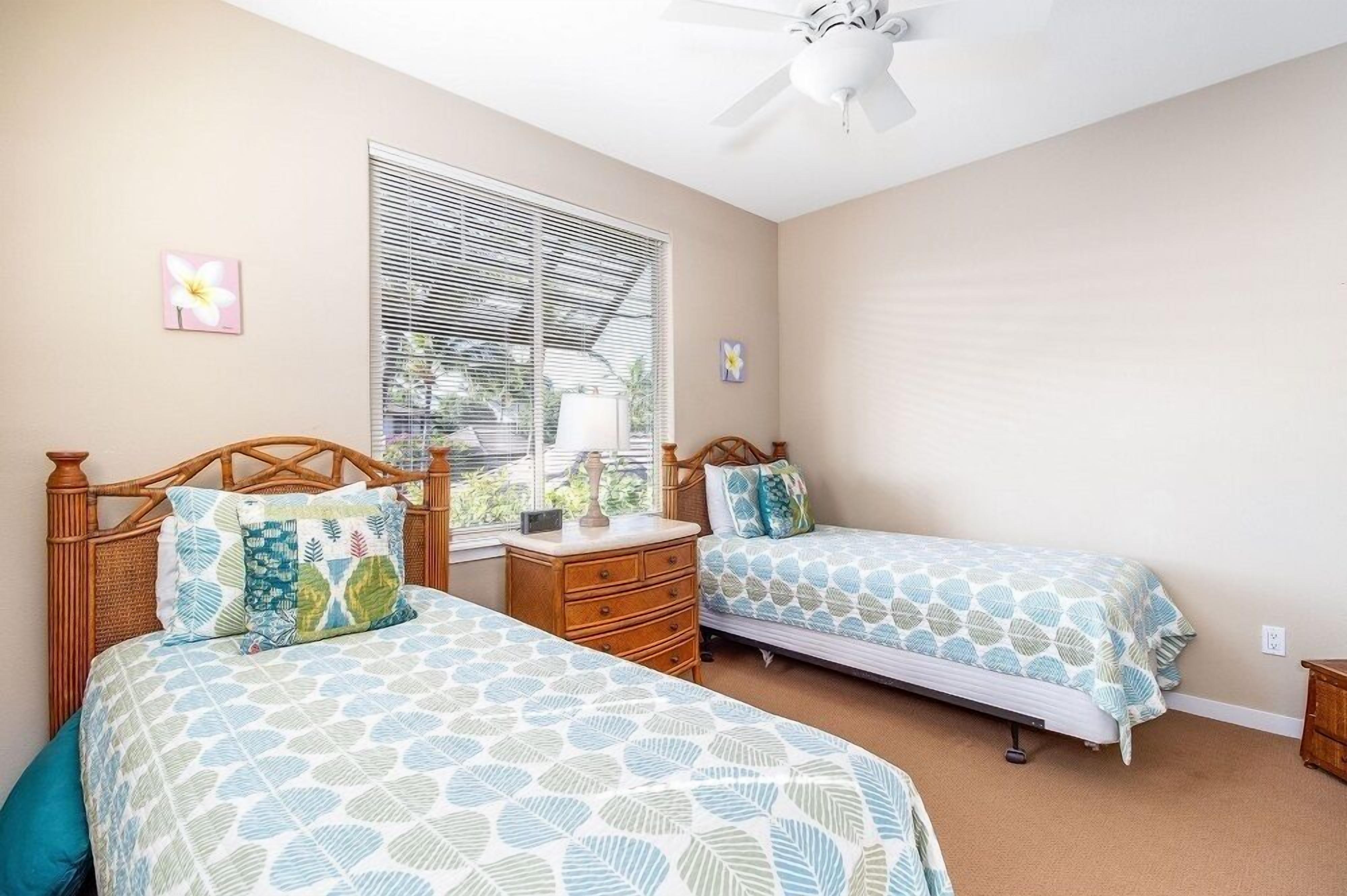 A bedroom with two beds, a ceiling fan, a window with blinds, and a small nightstand.