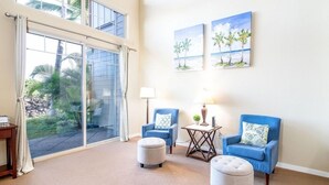 A spacious room with a large sliding glass door leading to a balcony, two blue armchairs with ottomans, a small table with a lamp, and two beach-themed paintings on the wall. - Includes Mauna Lani Beach Club Pass.  Golf Villa at Mauna Lani D3 (Waimea)