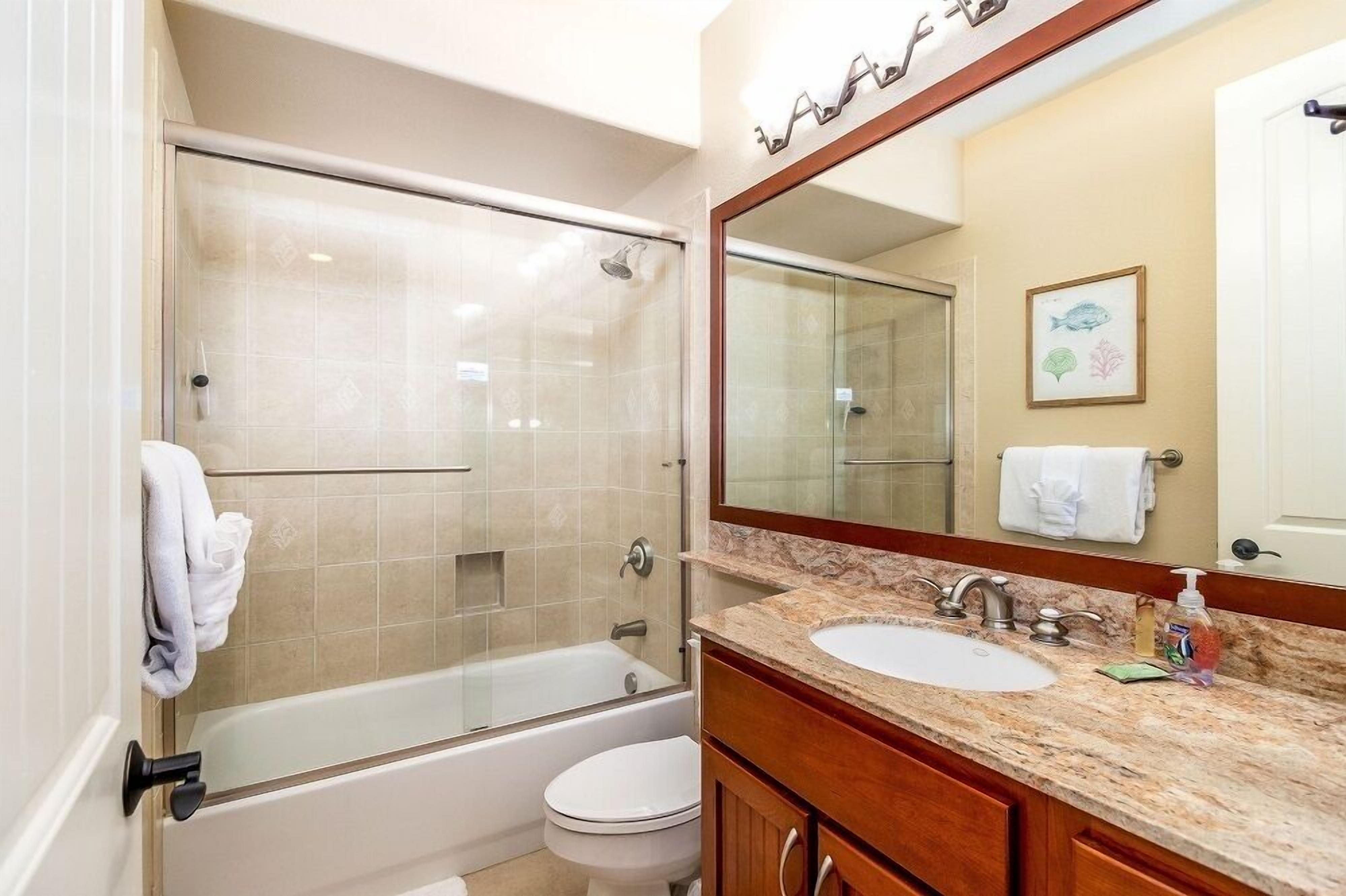 A bathroom with a glass-enclosed shower, a bathtub, a toilet, and a sink with a large mirror above it.