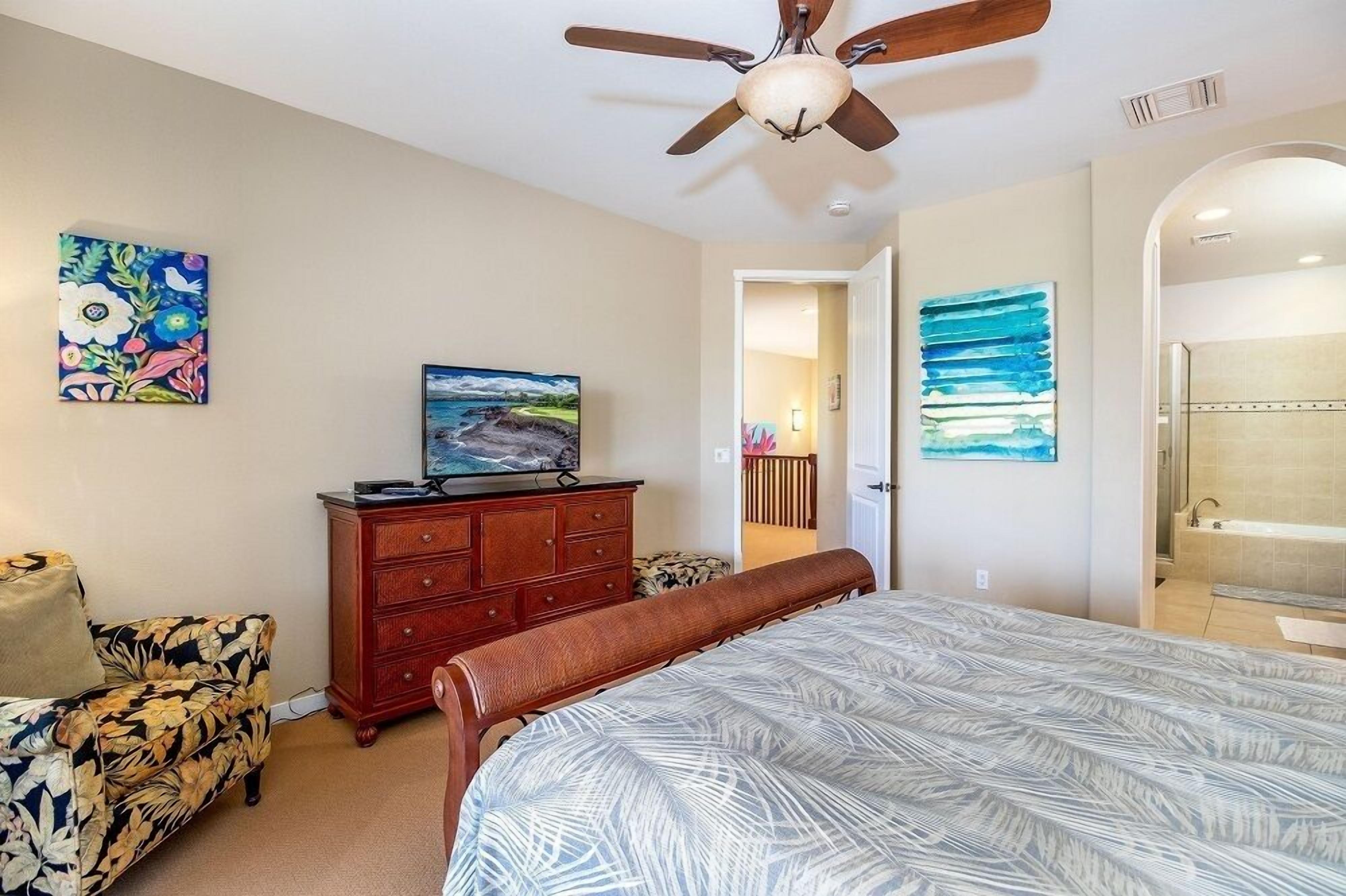 Une chambre à coucher avec un lit, un ventilateur de plafond, une commode, un téléviseur et des œuvres d’art accrochées aux murs.