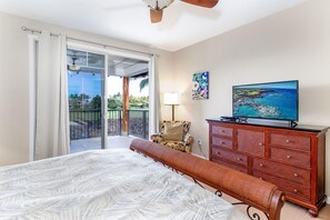 A bedroom with a bed, a dresser, a chair, a TV, and a balcony with a view of the ocean.