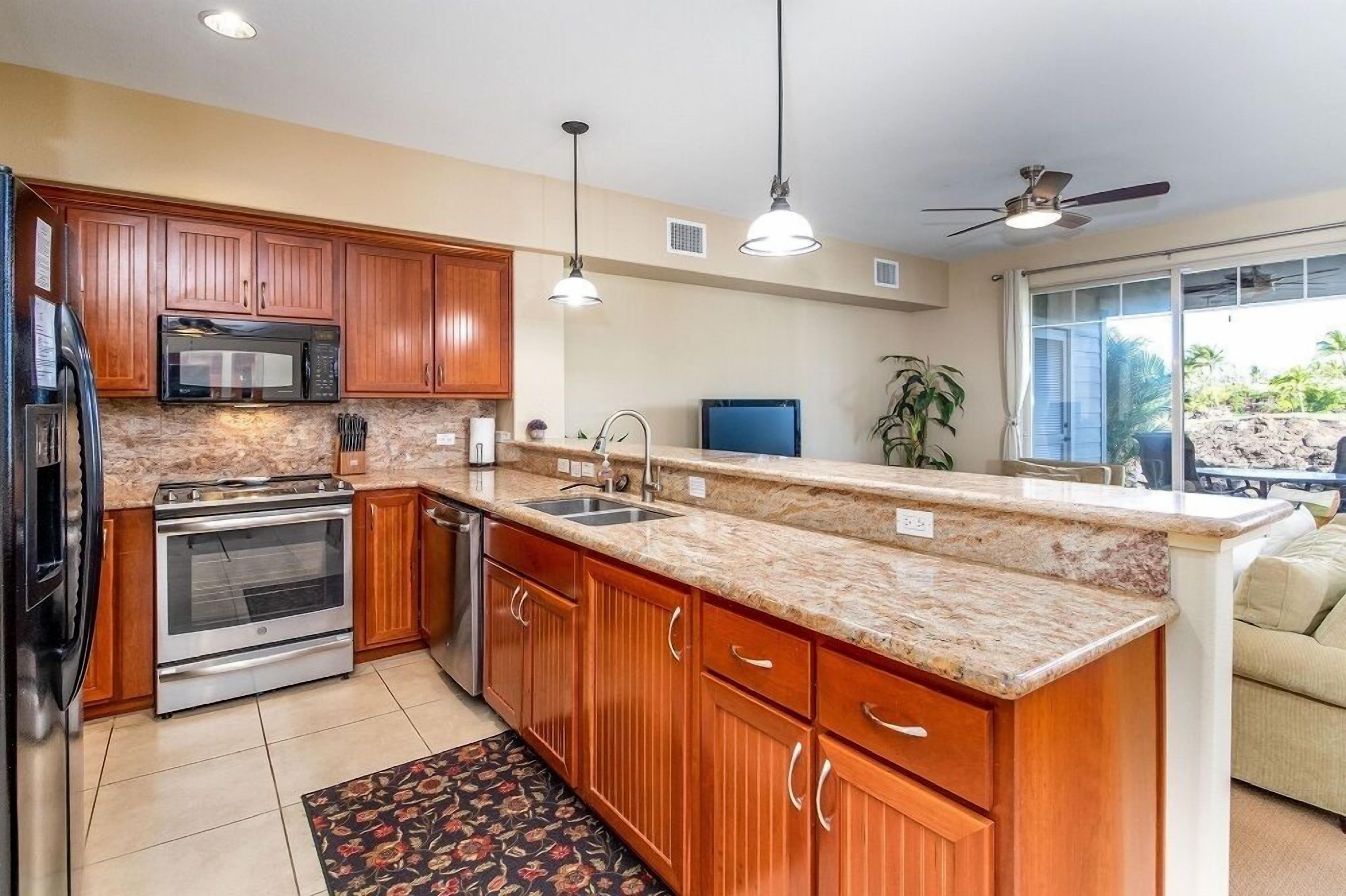 A kitchen with wooden cabinets, granite countertops, stainless steel appliances, pendant lighting, and a ceiling fan.