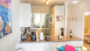 Eine kleine Küche mit Toaster, Wasserkocher und Kaffeemaschine auf der Arbeitsfläche. An der Wand hängt eine Uhr, und auf der Arbeitsfläche stehen zwei Flaschen.