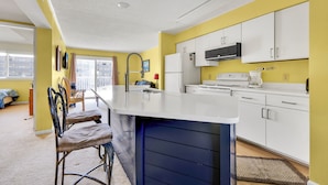 A modern kitchen with white cabinets, a central island, and a view to the living area. - Two bedroom, with pool, close to Seacrets! (Ocean City)