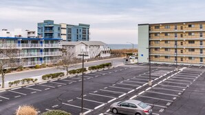 A parking lot with multiple rows of parking spaces, a building with balconies, and a view of the ocean in the background. - Two bedroom, with pool, close to Seacrets! (Ocean City)