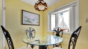 A dining area with a glass-top table surrounded by chairs, a painting on the wall, and a window with a sailboat view. - Two bedroom, with pool, close to Seacrets! (Ocean City)