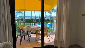 A room with a sliding glass door leading to an outdoor patio with a pool, wicker chairs, and a table set for dining. - Front line beach location with sea views. (Manilva)