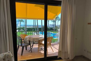 Une pièce dotée d’une porte-fenêtre coulissante donnant sur un patio extérieur avec une piscine, des fauteuils en osier et une table dressée pour le repas.