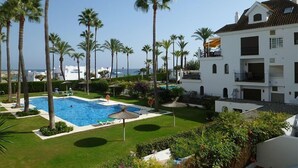 A pool area with palm trees, a white building, and a view of the sea. - Front line beach location with sea views. (Manilva)