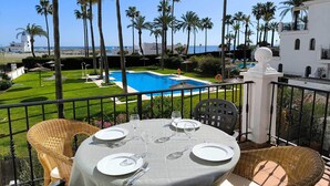 A balcony with a table set for dining, overlooking a swimming pool and palm trees. - Front line beach location with sea views. (Manilva)