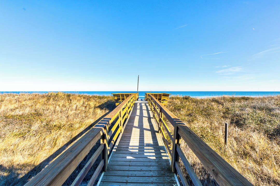 A wooden boardwalk leading to a beach with a clear sky.