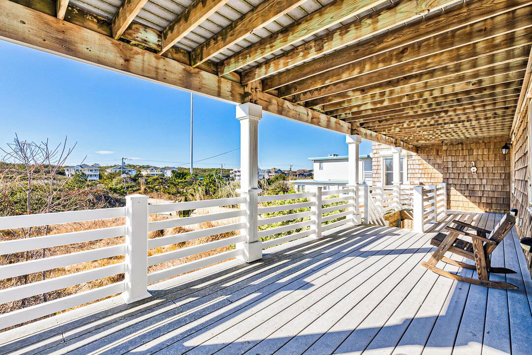 A wooden deck with white railings, a bench, and a covered area with a wooden ceiling.